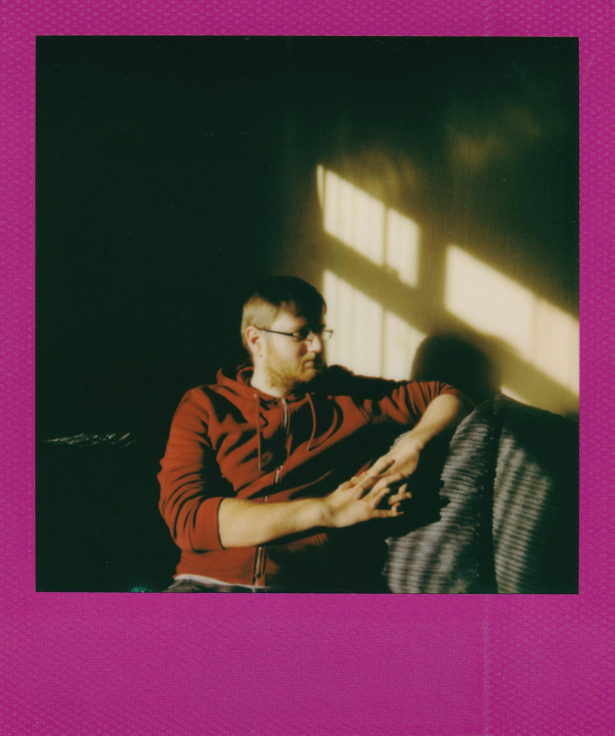 Man in red hoodie relaxing on sofa in soft indoor lighting, serene mood.