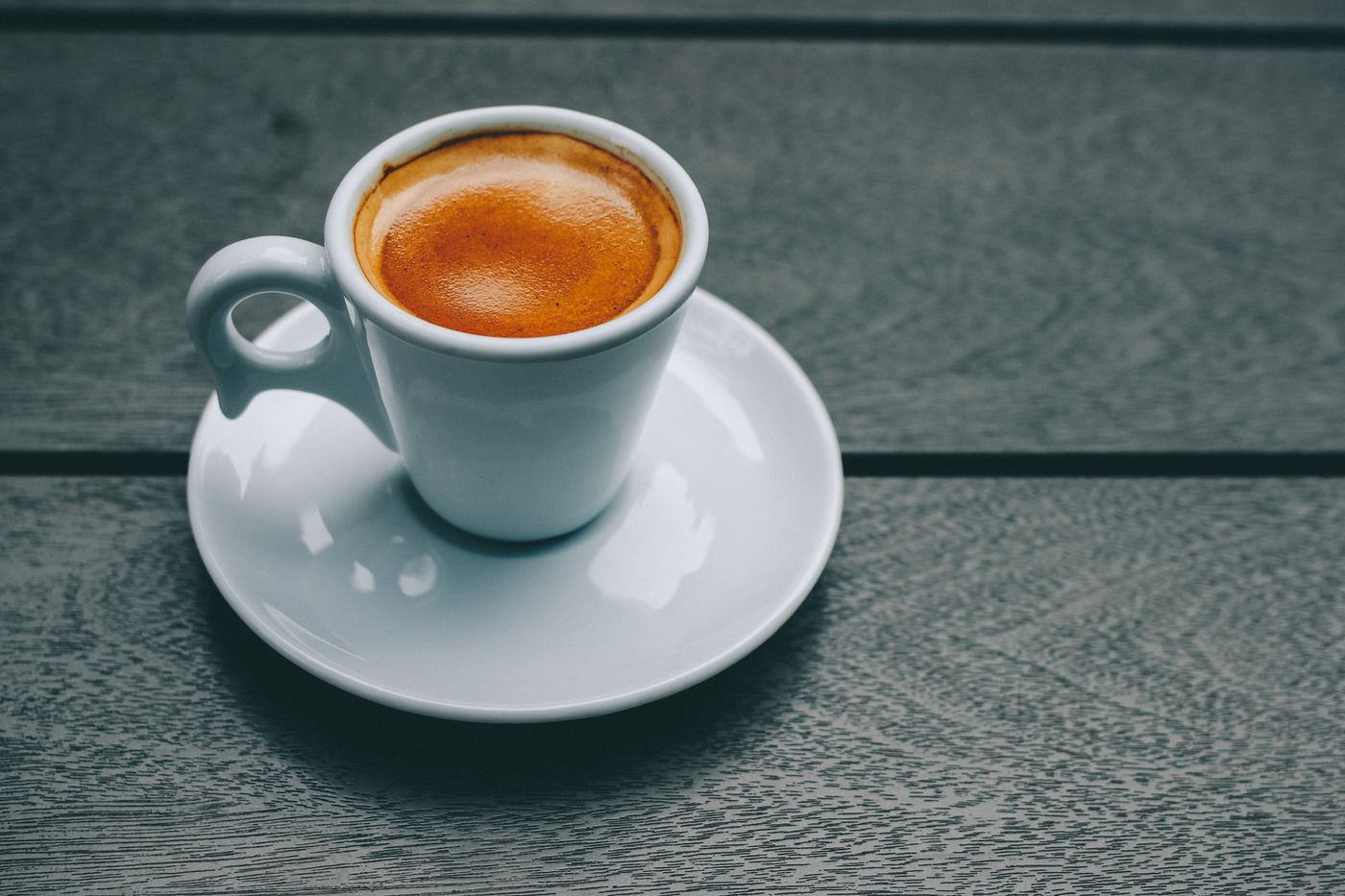 Taza blanca de espresso con una crema espesa y anaranjada sobre un plato.