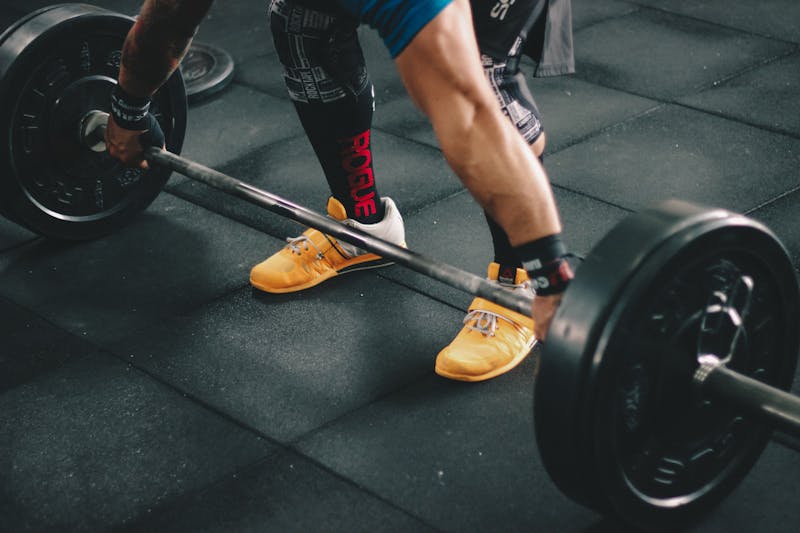 Person preparing to lift a barbell from the floor inside a well-equipped gym