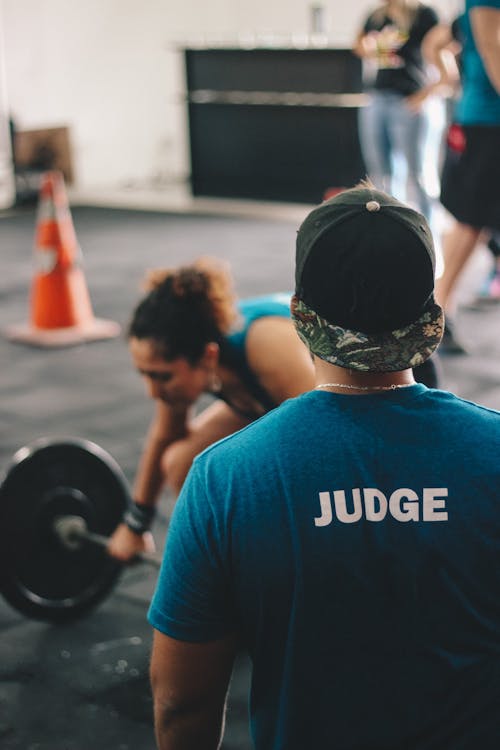 Free Man in Blue Crew-neck Shirt Staring At Woman Trying To Lift Barbell Stock Photo