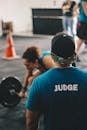 Man in Blue Crew-neck Shirt Staring At Woman Trying To Lift Barbell