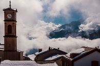 Clock tower with cross against foggy mountain in winter town