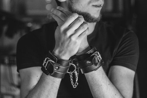 Free Close-up of a man's hands in leather cuffs, evoking themes of bondage and restraint. Stock Photo