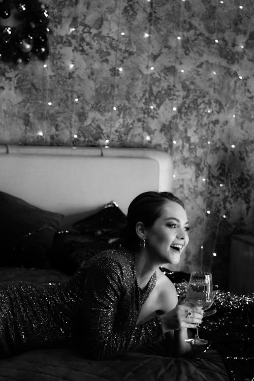 Happy lady in dress on bed with glass of champagne