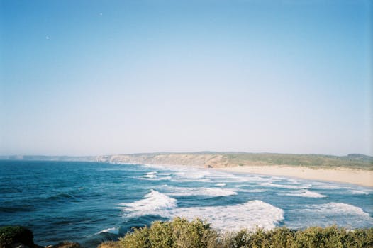 A scenic Portuguese coastline with waves crashing under a clear blue sky.