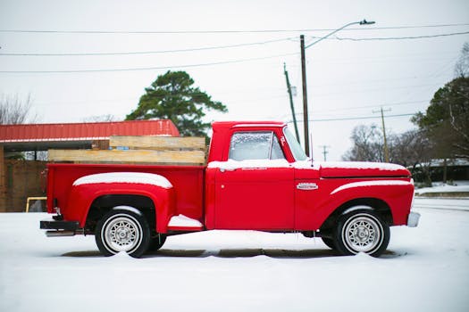 Bright vintage pick up truck parked on snowy terrain against construction and lamp post on winter day