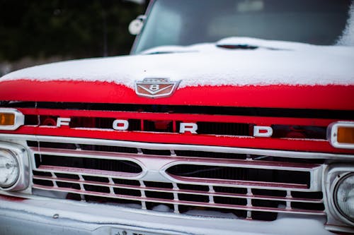 Bumper of vintage red pickup automobile with polished grille and snow on bonnet