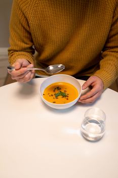 Man enjoying a bowl of pumpkin soup indoors, showcasing a cozy lifestyle setting.