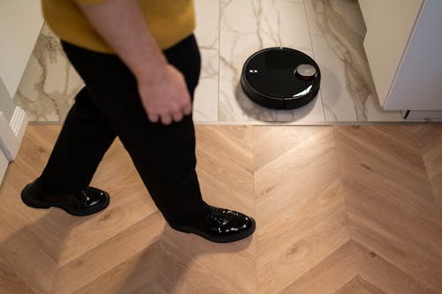 Person Walking Near a Robotic Vacuum Cleaner on Marble Floor