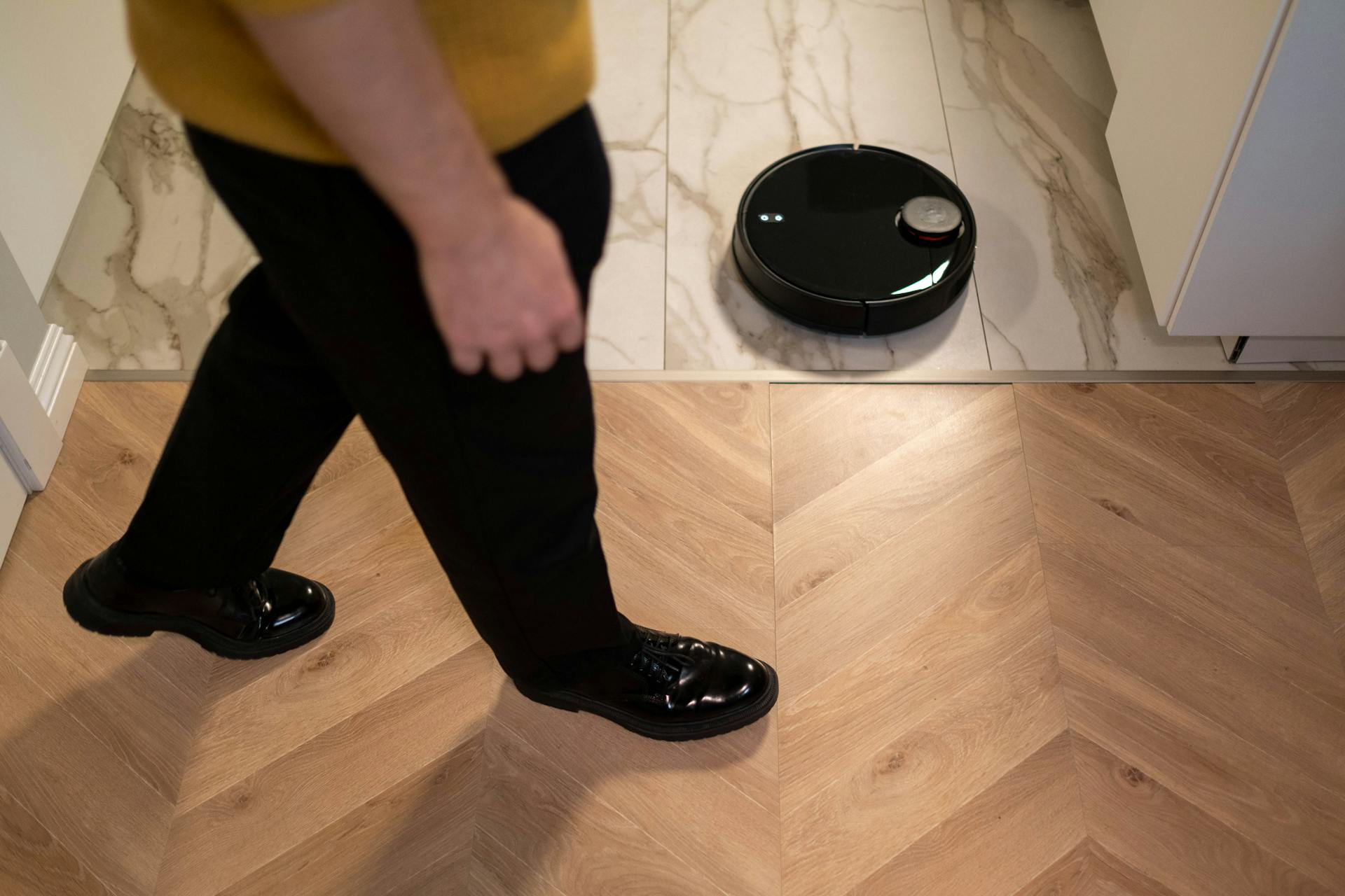 A robotic vacuum cleaner operating on a wooden floor, viewed in high angle indoor setting.