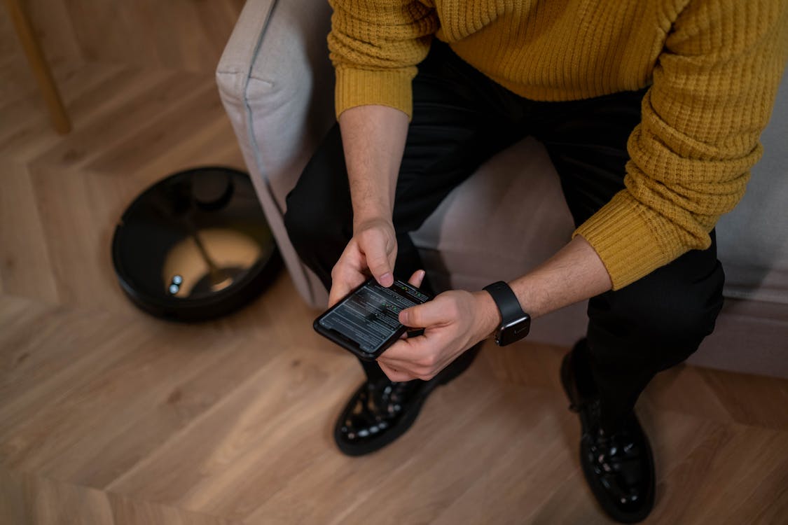 Free Person in Yellow Sweater and Black Pants Holding Black Smartphone Stock Photo