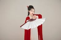 Woman in Red and White Long Sleeve Dress Holding a White Hand Fan