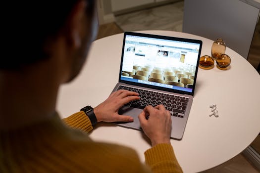 Individual in a yellow sweater using a laptop on a round table indoors.