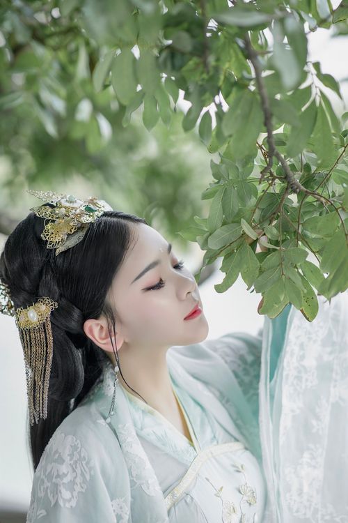 Free Elegant portrait of a woman in traditional hanfu attire amidst lush green leaves. Stock Photo
