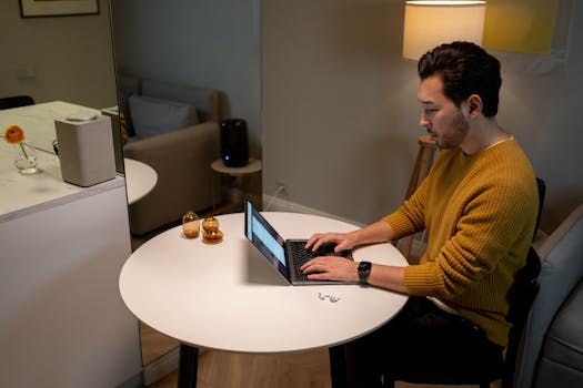 A man in a yellow sweater works on a laptop at home, creating a cozy and modern atmosphere.