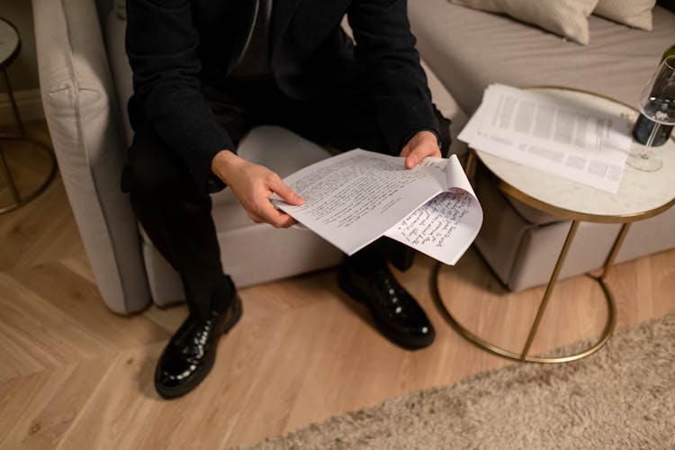 A Person In Black Suit And Leather Shoes Holding Stapled Papers