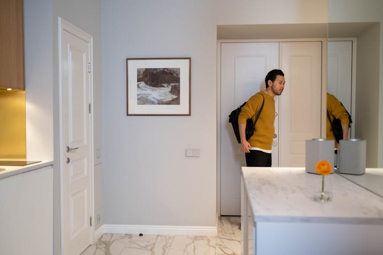 A Man In Yellow Sweater Carrying A Bag Standing Near A Door