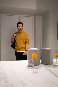 Asian man holding a bag in a modern room with flowers and decor.