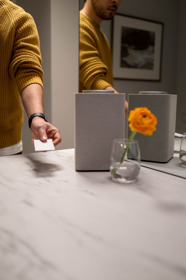 A Mirror Reflection Of A Man Standing Beside A Counter Holding A Card 