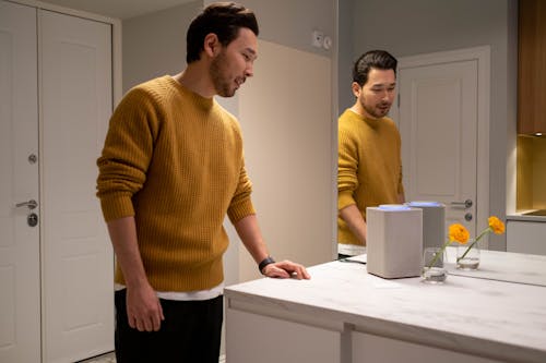 Photo of a Man in a Mustard Sweater Near a Mirror