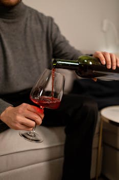 Close-up of red wine being poured into a glass indoors, creating a relaxing atmosphere.