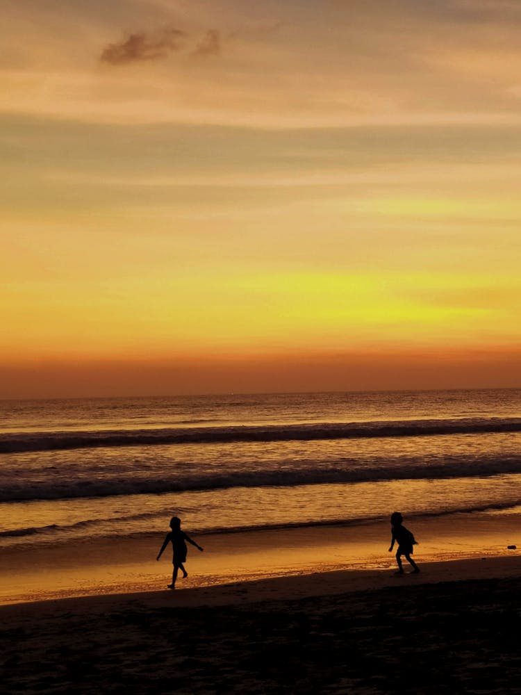 Silhouette Of Two Kids Running At The Beach During Sunset