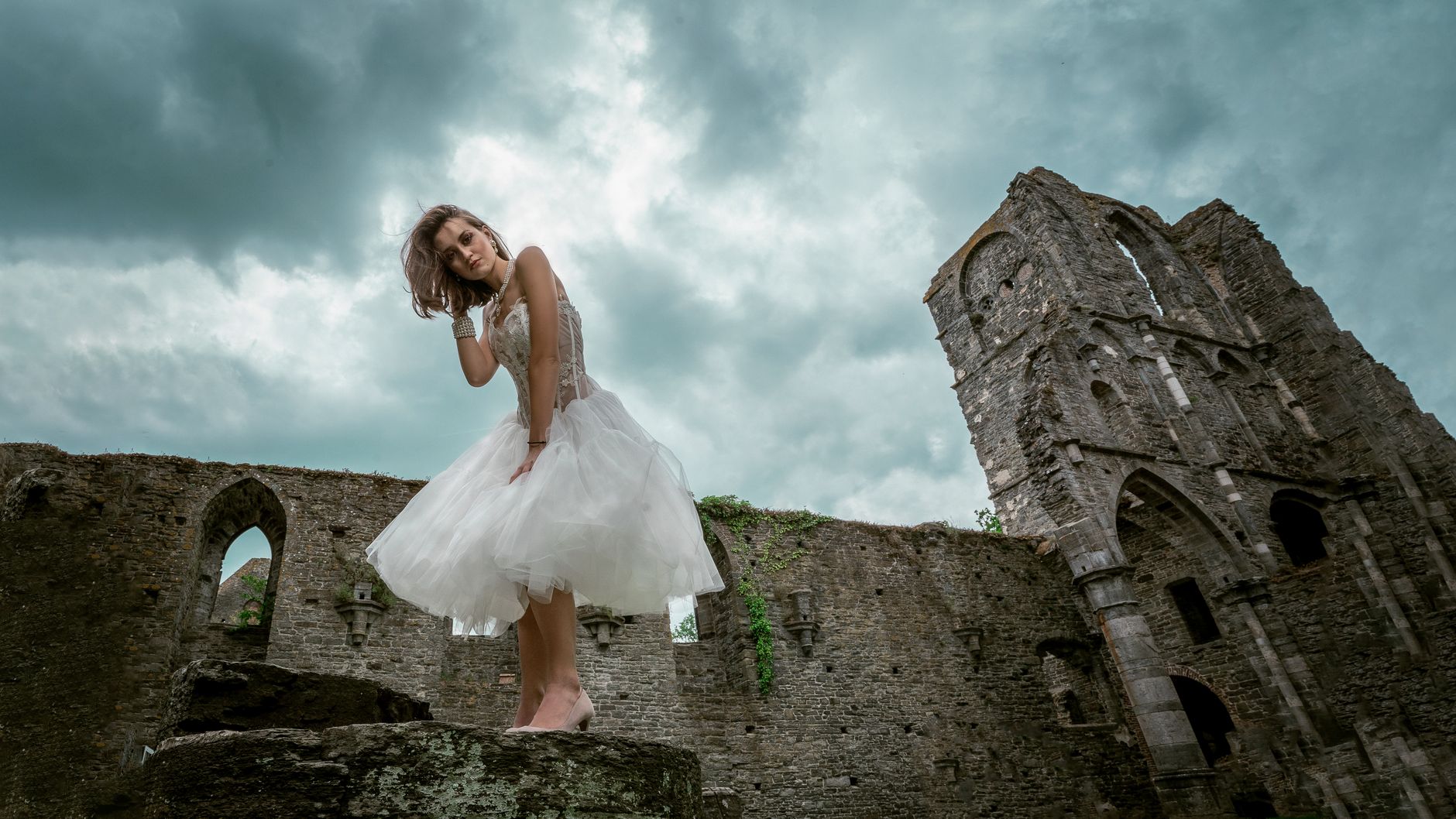 A beautiful bride poses elegantly in a historic castle ruin, emphasizing her dress.