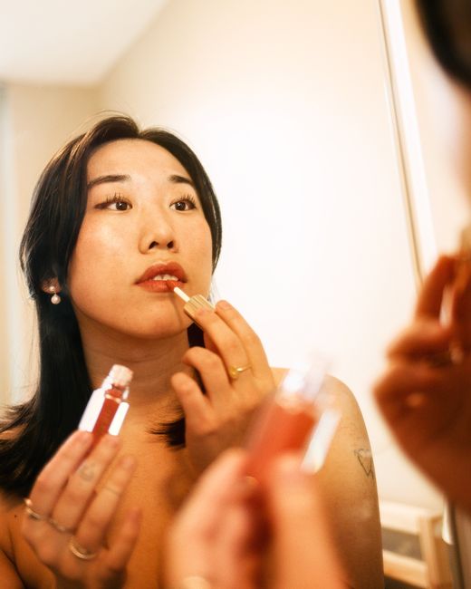 Asian female looking at mirror while applying lipstick