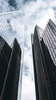 Low angle shot of modern skyscrapers in London with dramatic clouds reflecting on glass facades.