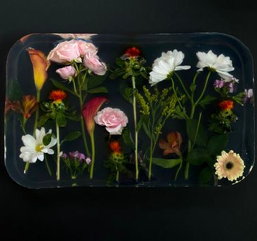 From above of composition of fresh blooming flowers in transparent epoxy resin placed on black surface