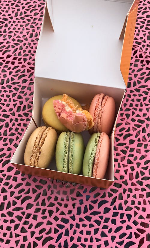 From above of cardboard container filled with delicious colorful macaroons placed on pink surface with black details