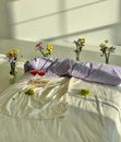 High angle of bed with pillows and glasses with wine near green grapes next to vases with bouquets of flowers on floor in light bedroom in daylight