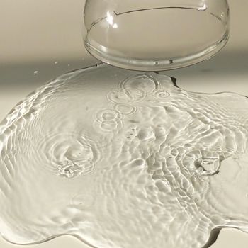 Transparent fragile inverted empty goblet near spilled clear water with ripples on white clean surface in light room with waterdrop