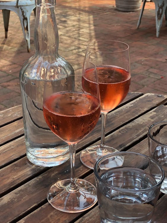 Glasses of delicious fine rose wine and cold water served on wooden table in outdoors restaurant