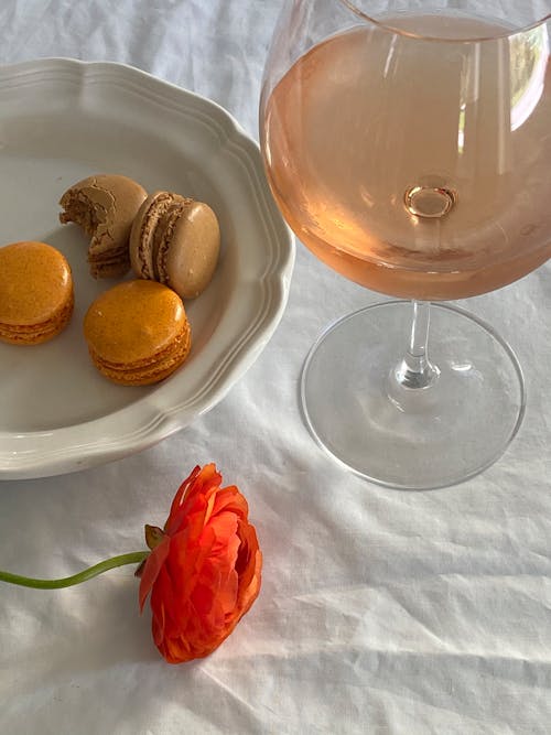 From above glass of delicious rose wine served on table near plate with yummy macaron cookies