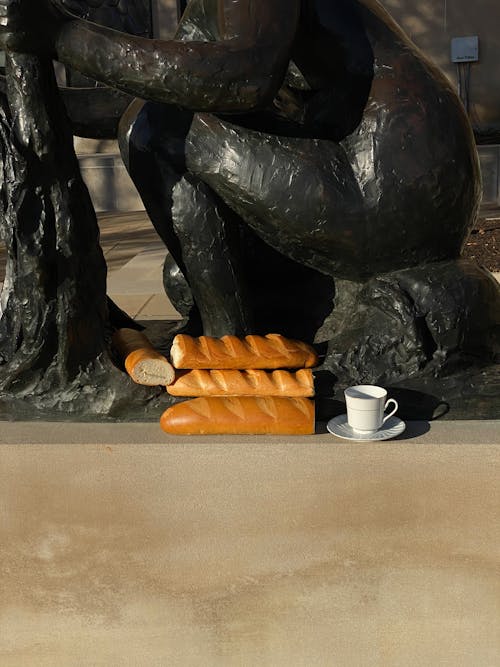 Free Fresh bread and coffee cup placed near statue on street Stock Photo
