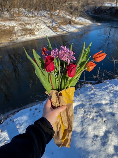 Faceless person holding bouquet of fresh flowers on snowy river shore
