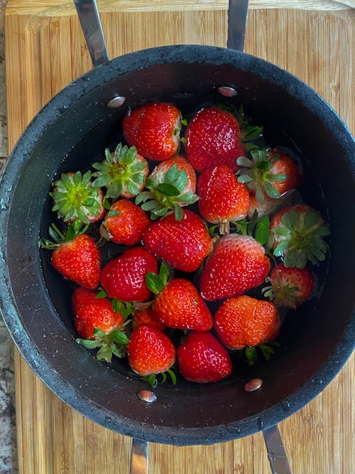 Top view of appetizing fresh ripe washed strawberries in bowl placed on wooden table in kitchen in daylight