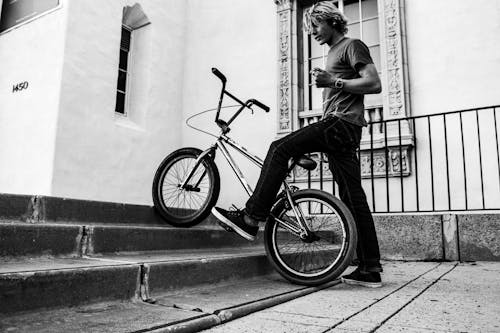 Grayscale Photo of a Man with a Bmx Bicycle Near Concrete Stairs