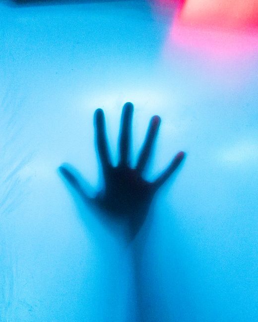 A striking shadow of a hand pressed against a translucent blue surface, conveying mystery and depth.