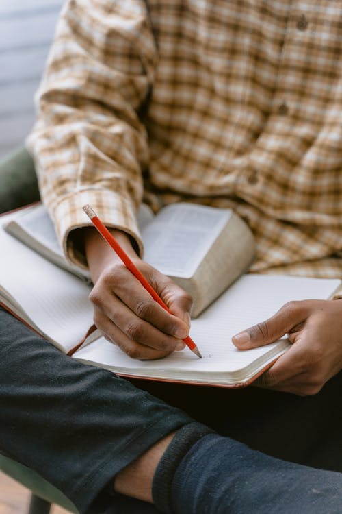 Person in Plaid Long Sleeves Writing on a Notebook 