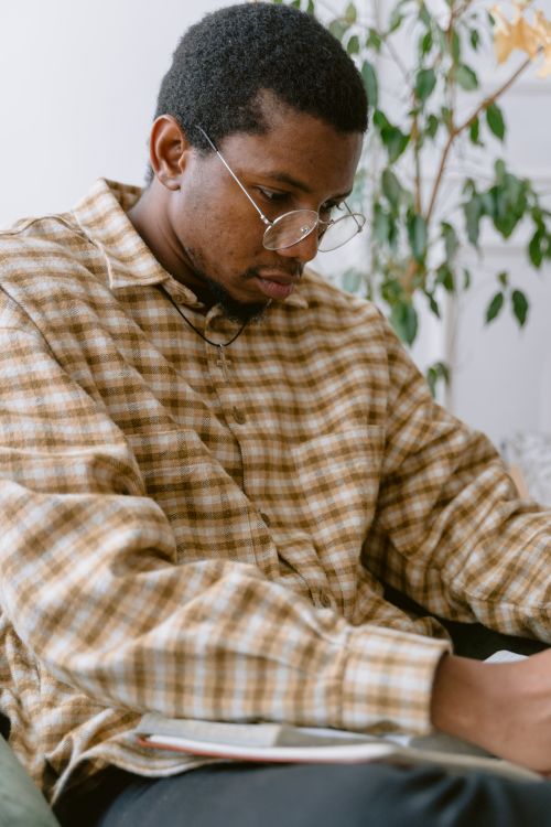 Free Young man with glasses writing indoors, focused and thoughtful in a cozy setting. Stock Photo
