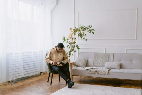 Free Man sitting and reading a book in a bright, minimalist living room. Stock Photo