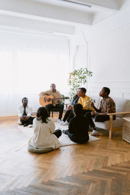 Free A diverse group of people praying and singing with a guitar in a cozy room setting, capturing a spiritual moment. Stock Photo