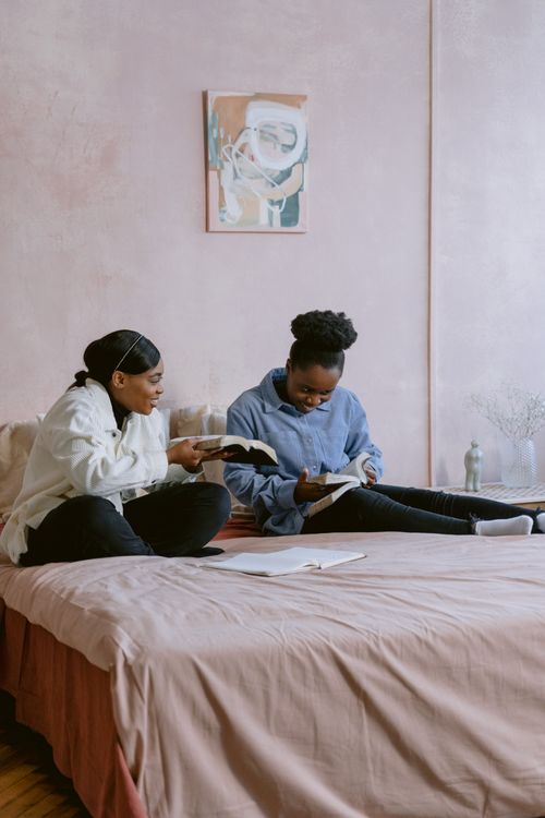 Free Two women relaxing on a bed, reading books together in a cozy indoor setting. Stock Photo