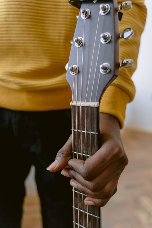 Free Detailed view of hand gripping the neck of an acoustic guitar indoors. Stock Photo
