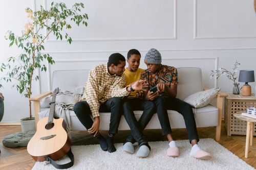 Free Three young men enjoying social media together indoors with a guitar nearby. Stock Photo