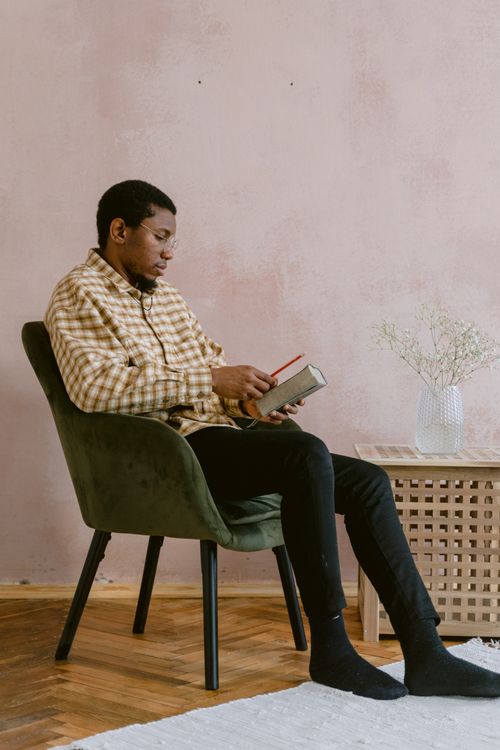 Free African American man reading in a chair, wearing plaid shirt, with a minimalist interior design. Stock Photo