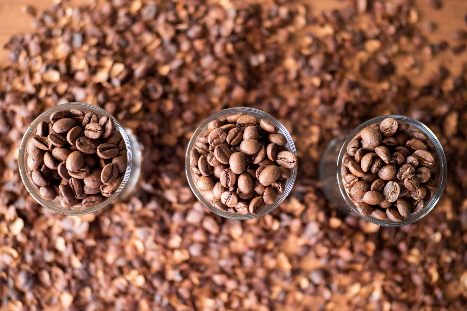 Close-up of roasted coffee beans in glass containers on a textured background, captured from above.