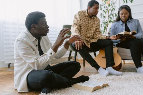 Free Three people engaged in a bible study discussion together inside a cozy room. Stock Photo